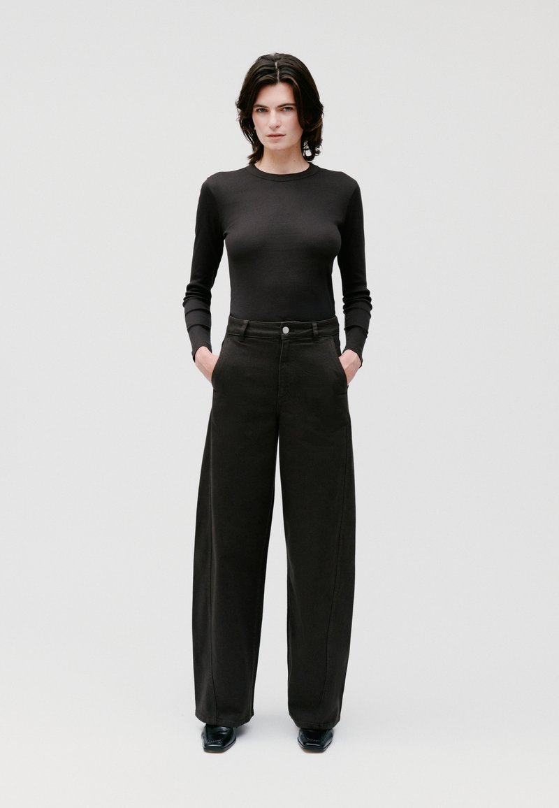 Top aderente a maniche lunghe nera abbinato a pantaloni neri a vita alta e gamba larga. Il materiale sembra morbido con una texture liscia; design minimalista.