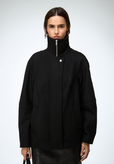 Sort frakk i uldblanding med høj krave, lynlås foran og trykknap. Har sidelommer og en afslappet pasform. Glat tekstur og struktureret design.