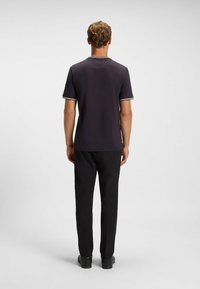 Dark short-sleeve t-shirt featuring contrasting white trim around the collar and sleeves, paired with dark, structured trousers and black shoes.