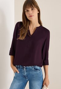 V-hals, langærmet bluse i mørk lilla, lavet af glat stof. Sammen med lyseblå denim jeans, der viser en afslappet pasform.