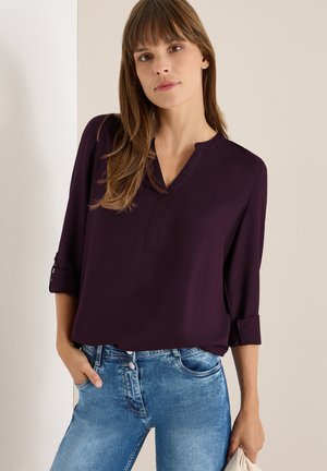 V-hals, langærmet bluse i mørk lilla, lavet af glat stof. Sammen med lyseblå denim jeans, der viser en afslappet pasform.
