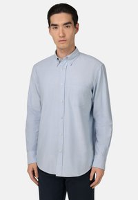 Chemise boutonnée bleu clair, à manches longues, en tissu mélangé de coton, avec une poche poitrine unique, ourlet arrondi, texture subtile, col classique.