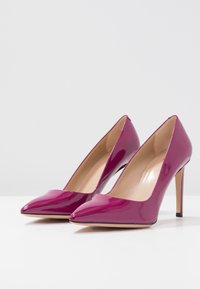 Escarpins magenta brillants avec un bout pointu et un talon aiguille élancé. Texture lisse, intérieur avec une doublure beige et aucun élément métallique visible.