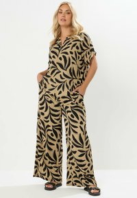 Mönstrad byxdress med vida ben i beige med svarta bladmönster, med korta ärmar, krage och framfickor; texturerad tyg.