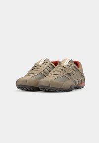 Beige sportsko med mesh- og semsket skinnmaterialer, med grå detaljer, rund tå, teksturert gummisåle, og logo-merke på tungen.