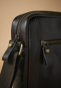 Dark brown leather bag with a textured surface, featuring a zipper on top, brass hardware, and a detachable woven strap.