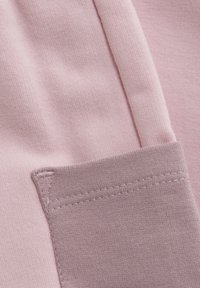 Ljusrosa tyg med en slät, strukturerad yta; har en grå accentficka med synliga stygn längs kanten.