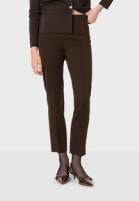 Bruna skräddarsydda byxor med en figurnära passform, mjuk textur och slät yta, kombinerade med bronsfärgade slingback-klackar.