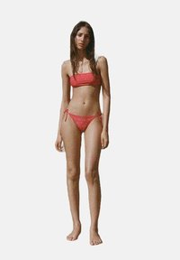 Röd tvådelad bikini med bandeau-top och låga slips. Utsmyckad med små dekorativa inslag. Slät textur och justerbara snören.