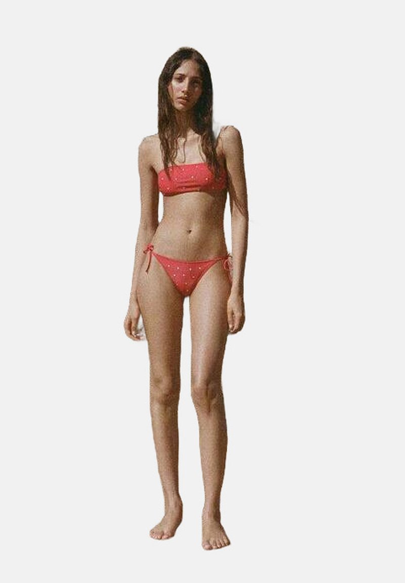 Röd tvådelad bikini med bandeau-top och låga slips. Utsmyckad med små dekorativa inslag. Slät textur och justerbara snören.