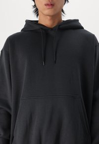 Haut à capuche noir fabriqué en tissu doux, avec une poche avant, des cordons de serrage réglables et une coupe décontractée, avec des détails de couture minimalistes.
