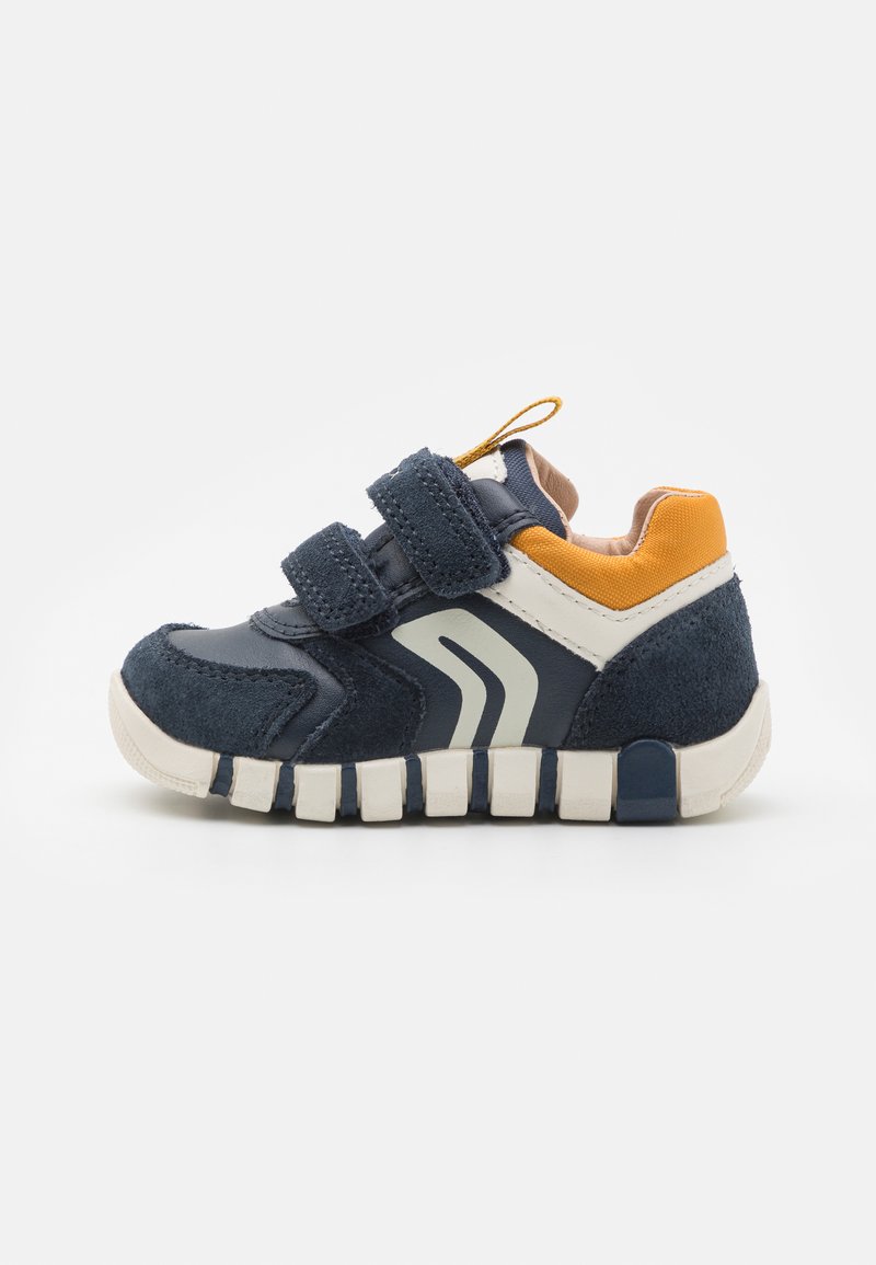 Sneaker per bambini blu e navy con due cinturini in velcro, dettagli in suede, suola in gomma testurizzata e dettaglio arancione sul tallone. Logo stilizzato bianco.