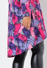 Tunic colorato con un motivo di volti astratti in viola, rosa e nero, realizzata in morbido tessuto con maniche lunghe, abbinata a leggings neri lucidi.