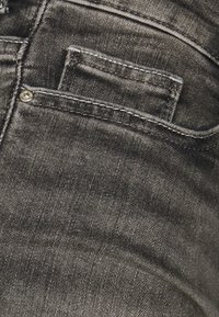 Jean en denim noir avec une petite poche avant, des coutures discrètes et une texture lisse, avec un léger brillant et un design à coupe classique.