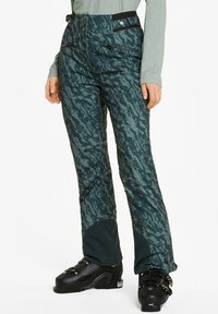 Ski broeken in donkergroen met een gestructureerd golfpatroon, hoge taille, twee zakken met rits en een verstevigde onderkant, gecombineerd met zwarte skibotten.