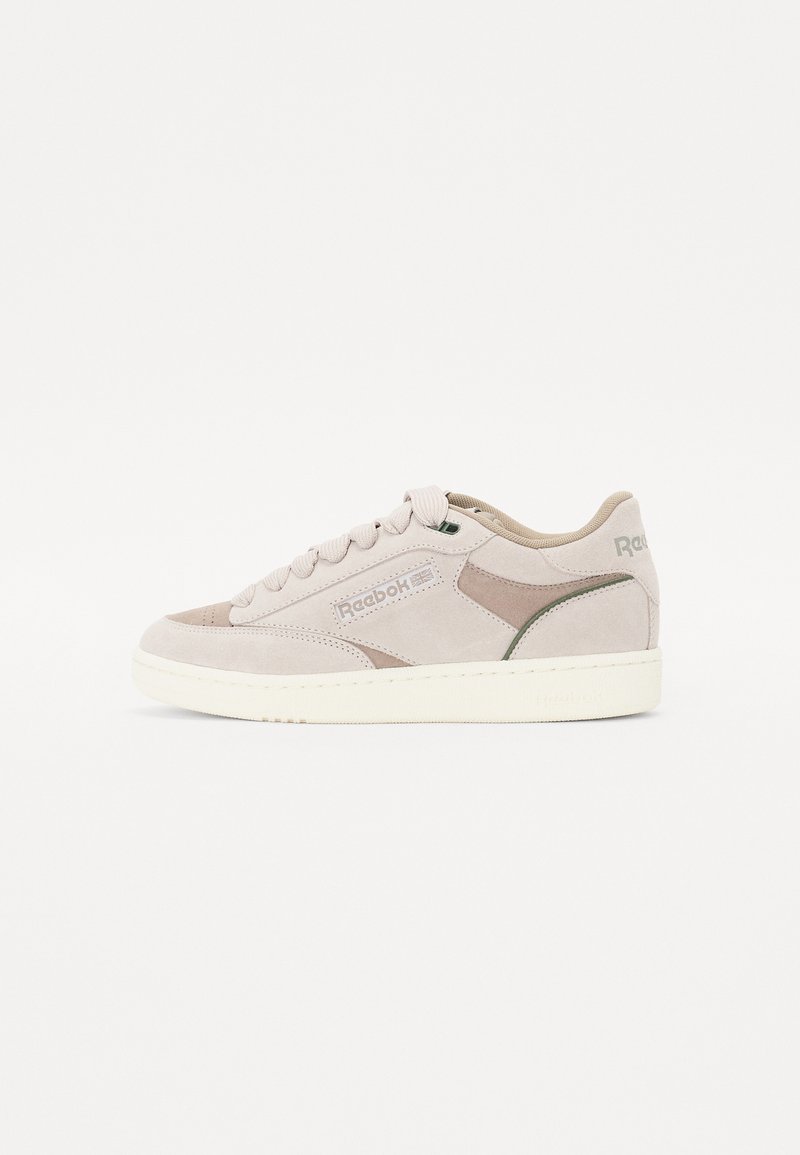 Sneakers with a suede upper in light beige, featuring a cream rubber sole, round laces, and a subtle green accent on the heel.