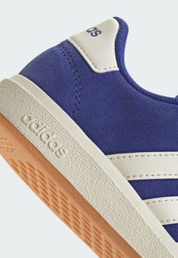 Baskets en daim bleu avec des rayures en cuir blanc, semelle en caoutchouc beige texturé, arborant un logo en relief et des surpiqûres contrastées au niveau du talon.