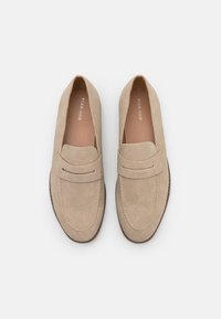 Mocassins en daim beige à texture lisse, avec un détail surpiqué sur le cou-de-pied et un talon modeste pour un soutien supplémentaire.