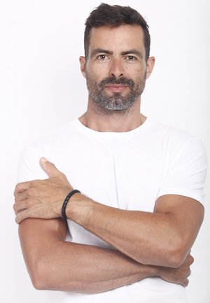 Model in a plain white t-shirt with short sleeves, resting arms crossed. Wears a black braided bracelet on the left wrist.