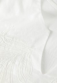 White fabric featuring intricate white embroidery of flowing, leaf-like shapes. Smooth texture with detailed stitching accents.