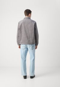 Grå kordfløjljakke med en afslappet pasform, med krave og elastiske manchetter, parret med lyseblå lige jeans og sorte sko.