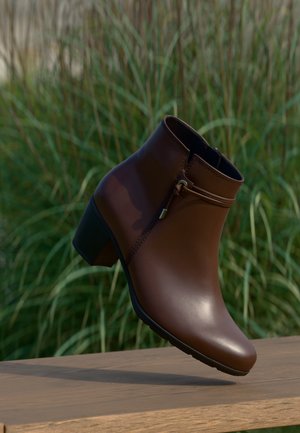 Brauner Lederknöchelstiefel mit niedrigem Blockabsatz und seitlichem Reißverschluss, im Freien auf einer Holzoberfläche mit grünen Pflanzen im Hintergrund präsentiert.