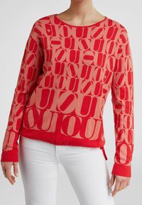 Suéter con patrón en rojo y rosa claro, mangas largas, escote redondo y diseño decorativo de letras. Presenta un corte ligeramente cropped.