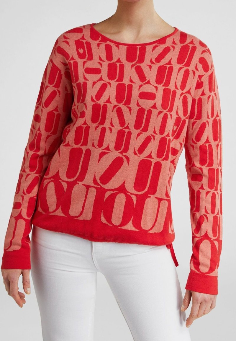 Suéter con patrón en rojo y rosa claro, mangas largas, escote redondo y diseño decorativo de letras. Presenta un corte ligeramente cropped.