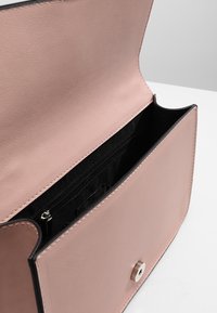 Světle růžová kožená kabelka otevřená, aby ukázala černý interiér s zipovou kapsou a stříbrným magnetickým uzávěrem na předním klapce.
