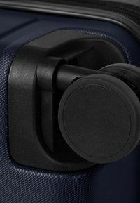 Primer plano de una rueda giratoria negra de una maleta, adherida a un equipaje rígido de color azul oscuro con textura.