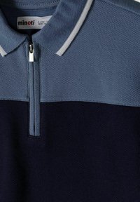 Polo à manches courtes bleu et marine avec des rayures blanches sur le col et une fermeture éclair à l'avant.