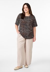 Top s krátkým rukávem s leopardím potiskem v černé a tan barvě, spárovaný se světle béžovými širokými kalhotami a béžovými plochými botami. Hladká tkanina, uvolněný střih.