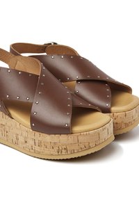 Bruine leren platform sandalen met gekruiste banden, zilveren studs en een natuurlijk kurk-textuur platform. Rondte neus en verstelbare band.