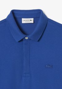 Blå piké skjorta i strukturerad tyg, med klassisk krage, tre-knapplåsning och broderad logotyp på bröstet.