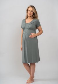 Těhotenské šaty z jemné, světle zelené látky, s krátkými rukávy, výstřihem do lodičky a designem v empírovém stylu pro pohodlí.