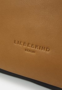 Sac en cuir brun à texture présentant un panneau inférieur noir avec le logo embossé "LIEBESKIND BERLIN". La finition lisse souligne la durabilité.