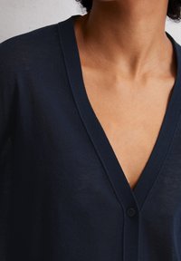 Cardigan léger bleu marine avec un col en V, doté d'une fermeture à un bouton et d'une texture subtile, présenté du col vers le bas.