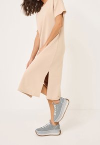 Abito di cotone beige con maniche corte e spacchi laterali, abbinato a sneakers in suede grigio con una spessa suola bianca e battistrada marrone.
