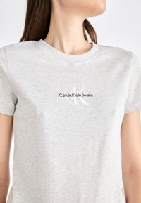 Svijetlosivi pamučni majica s okruglim izrezom i kratkim rukavima, sa vezanim logotipom "Calvin Klein Jeans" u crnoj i bijeloj boji.