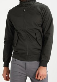 Ciemnozielona kurtka bomberka z zamkiem z przodu, stojącym kołnierzem i dwoma zapinanymi na guziki bocznymi kieszeniami; ściągacze na mankietach i u dołu. Gładka, trwała tkanina.