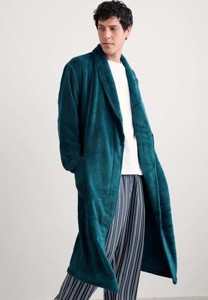 Tyrkis flanellrock med långa ärmar, sjalkrage och sidofickor; bärs över vit skjorta och randiga pyjamasbyxor. Slät textur.