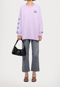 Camiseta de manga larga lavanda con estampado gráfico, combinada con jeans acampanados gris claro, bolso negro y sandalias negras con tiras.