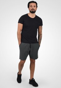 Black short-sleeve t-shirt with a chest pocket, paired with charcoal gray shorts. Model wears black athletic shoes. Simple, casual design.