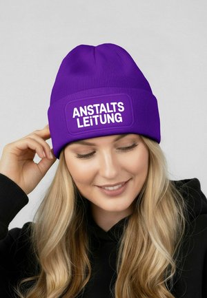 Purple knit beanie with a ribbed texture, featuring a rectangular white patch displaying the text "ANSTALTSLEITUNG."