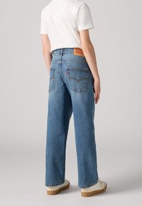 Ljusblå denimjeans med hög midja, vida ben, som har två bakfickor och en tanfärgad läderlogg i midjan.