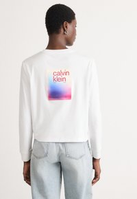 Felpa corta bianca con una grafica quadrata a gradiente colorato e il testo "calvin klein" sulla schiena. Tessuto morbido e liscio.