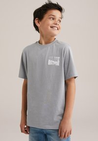 Pelēks kokvilnas T-krekls ar īsām piedurknēm, apaļu kaklu un balti izdrukātu tekstu "BLUE RIDGE" kreisajā krūšu daļā. Maiga tekstūra.