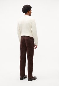 Cremefarvet ribbet sweater og mørkebrune fløjlssbukser med sidelommer og en afslappet pasform. Materialets tekstur er synlig i begge beklædningsgenstande.