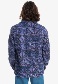 Pile con motivo geometrico in viola, blu e nero. Presenta un colletto e maniche lunghe. Tessuto morbido, vestibilità comoda.