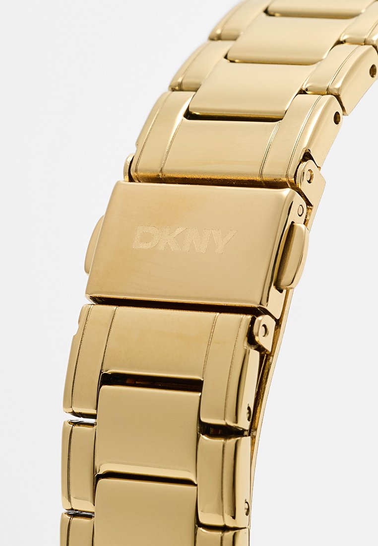 Goldfarbene Metalluhr mit einem Gliederarmband-Design. Sie verfügt über glatte, polierte Oberflächen und einen Verschluss, der mit "DKNY" graviert ist.
